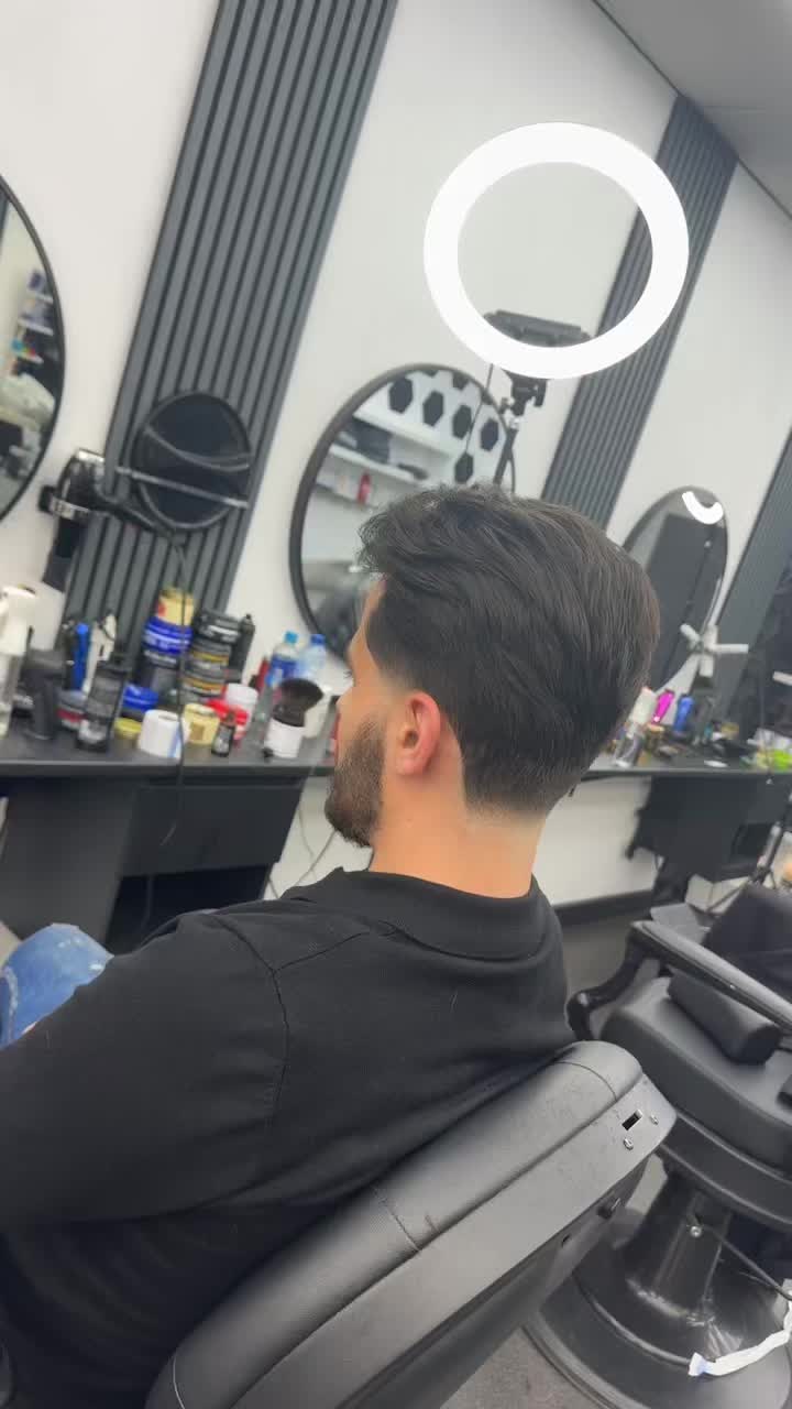 Klant in de stoel na knippen met baard, met de ringlamp en de spiegels van de zaak