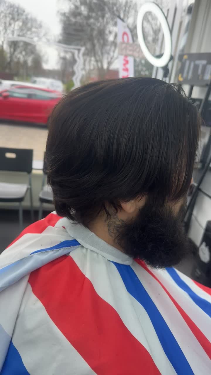 Lang haar en een volle baard, klant in een gestreepte kapperscape